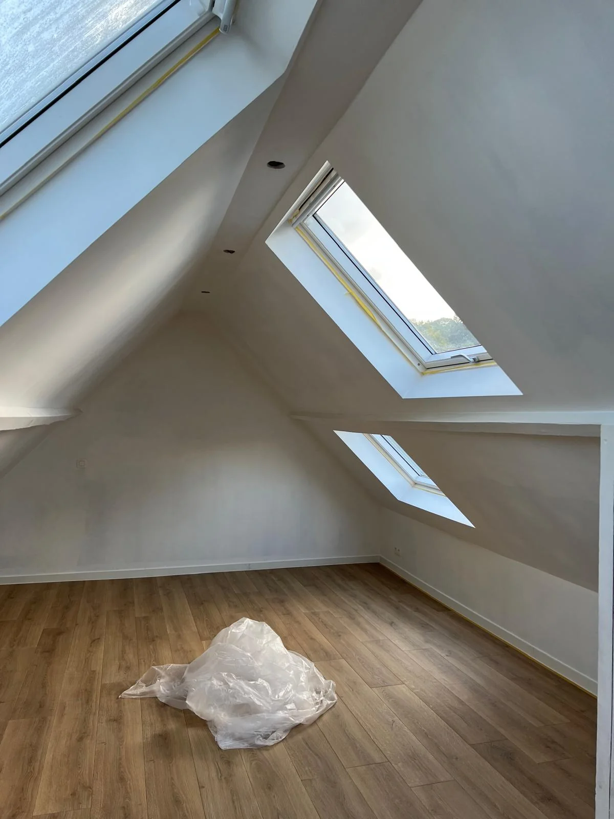 Combles aménagés à Woluwe-Saint-Pierre Espace sous toiture avec parois claires, plusieurs fenêtres de toit et sol aspect bois.