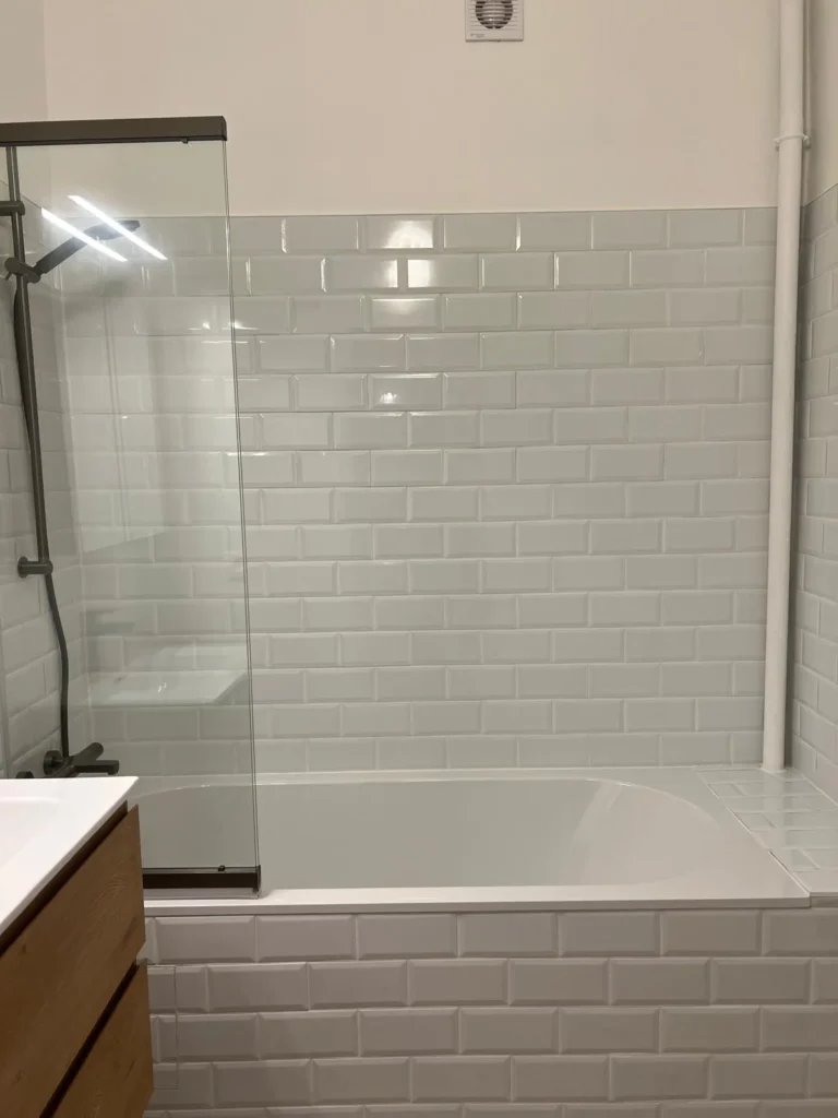 Baignoire blanche avec pare-baignoire vitré et habillage en carrelage métro.