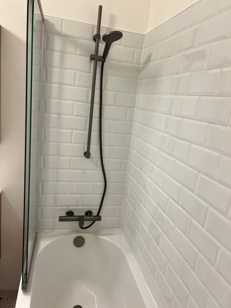 Robinetterie foncée et douchette au-dessus d’une baignoire entourée de carrelage métro blanc.