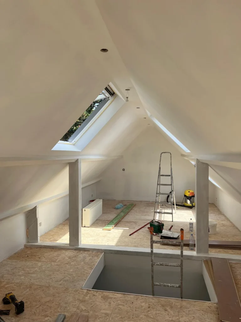Combles en cours d’aménagement avec parois claires, trémie et matériel de chantier.