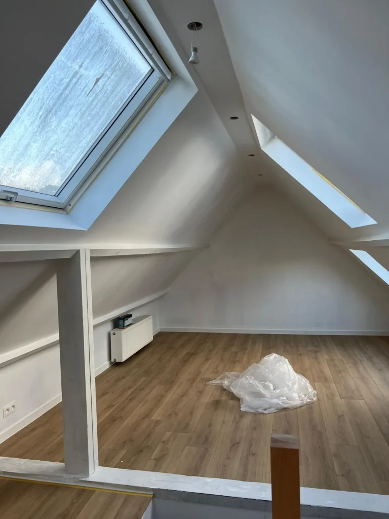 Vue des combles avec rampants clairs, fenêtres de toit et poteau au premier plan.
