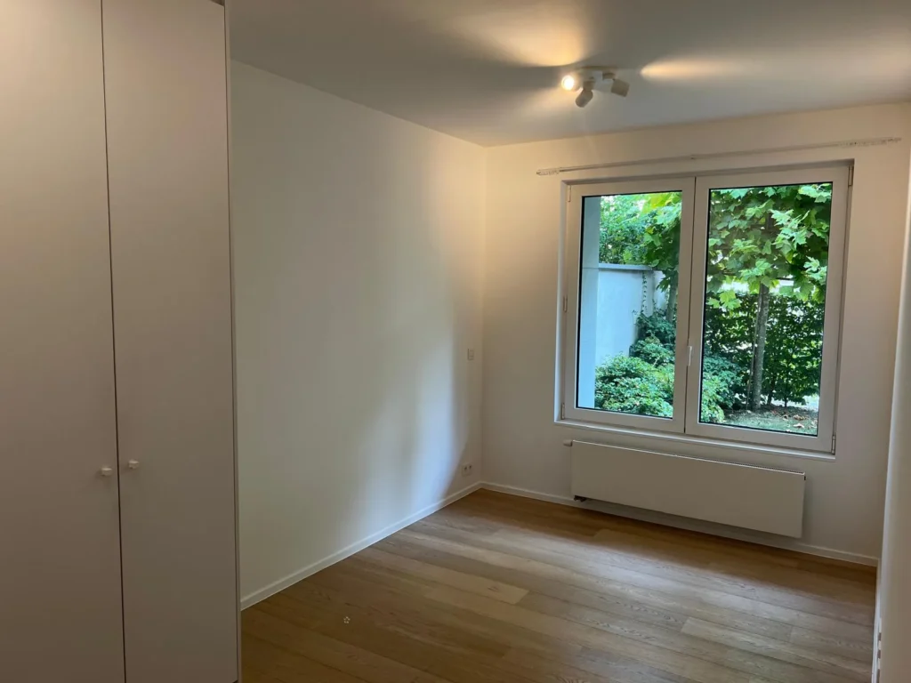 Chambre aux murs clairs avec placard intégré, fenêtre et radiateur.