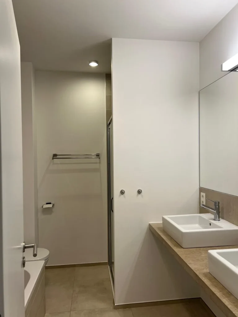Surfaces murales claires dans une salle de bain avec vasques, miroir et douche.